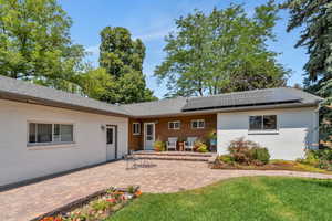 Back of house featuring brick siding, solar panels, a patio, a lawn, and a shingled roof