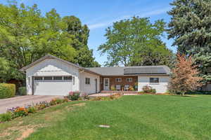 Single story home with board and batten siding, a front yard, an attached garage, roof mounted solar panels, and brick siding