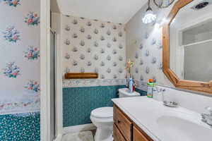 Full bath featuring wallpapered walls, vanity, and a stall shower