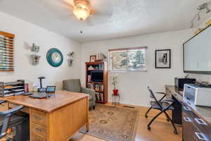 Home office with light wood-style flooring and a textured ceiling