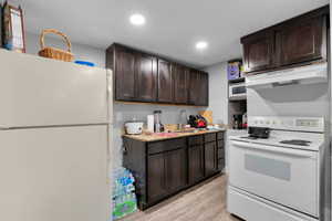 Kitchen featuring white appliances, dark brown cabinets, light wood-style floors, under cabinet range hood, and recessed lighting