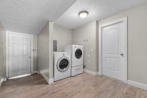 Washroom featuring washer and dryer, a textured ceiling, and light wood finished floors
