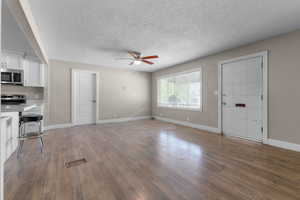 Unfurnished living room with a textured ceiling, wood finished floors, and a ceiling fan