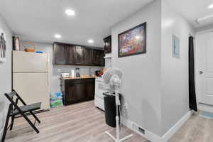 Kitchen with white appliances, dark brown cabinets, recessed lighting, light wood-type flooring, and light countertops