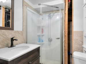 Bathroom featuring vanity, a textured ceiling, a stall shower, tile walls, and backsplash