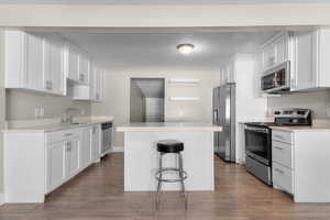 Kitchen with appliances with stainless steel finishes, white cabinets, a center island, wood finished floors, and a textured ceiling