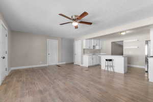 Unfurnished living room with a textured ceiling, a ceiling fan, and light wood finished floors