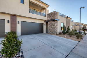 Modern home featuring stone siding, stucco siding, an attached garage, a balcony, and driveway