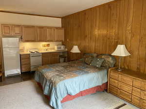 Bedroom featuring wood walls, freestanding refrigerator, crown molding, and dark colored carpet