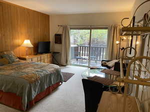 Bedroom with access to outside, wooden walls, and light colored carpet