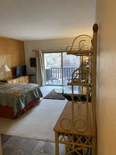 Carpeted bedroom with stone tile flooring, wood walls, and access to outside
