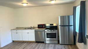 Kitchen featuring stainless steel appliances, white cabinetry, light countertops, and light wood-style floors