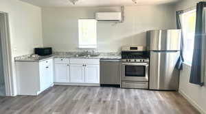 Kitchen with appliances with stainless steel finishes, white cabinetry, a wall mounted AC, light stone countertops, and light wood finished floors