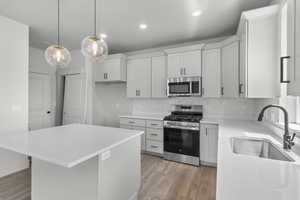 Kitchen featuring stainless steel appliances, light wood-style floors, a center island, tasteful backsplash, and light countertops