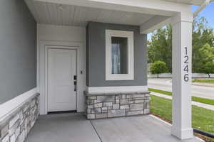 Doorway to property featuring stone siding, stucco siding, and a porch
