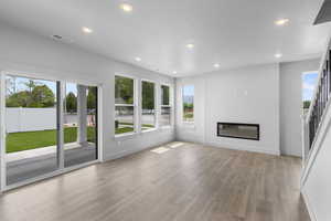 Unfurnished living room featuring a glass covered fireplace, wood finished floors, plenty of natural light, and recessed lighting