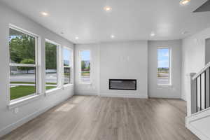 Unfurnished living room with recessed lighting, a glass covered fireplace, and light wood finished floors