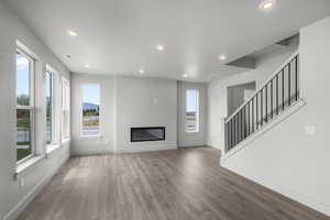 Unfurnished living room featuring a glass covered fireplace, stairway, wood finished floors, and recessed lighting