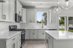 Kitchen with stainless steel appliances, light countertops, light wood finished floors, pendant lighting, and backsplash