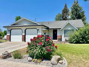 Single story home featuring brick siding, roof with shingles, a front yard, a garage, and driveway