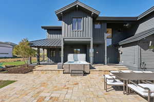 Rear view of property featuring board and batten siding, a patio area, a hot tub, and a standing seam roof