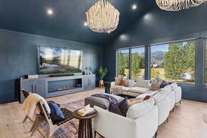 Living room with hardwood / wood-style flooring, a glass covered fireplace, recessed lighting, a chandelier, and high vaulted ceiling