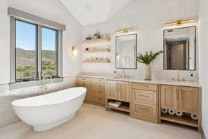 Full bath with tile walls, double vanity, a soaking tub, lofted ceiling, and backsplash