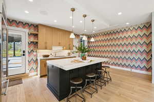Kitchen with wallpapered walls, hanging light fixtures, dark cabinetry, light wood finished floors, and a breakfast bar area