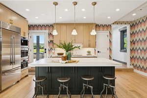 Kitchen featuring appliances with stainless steel finishes, decorative light fixtures, wallpapered walls, light wood-type flooring, and recessed lighting