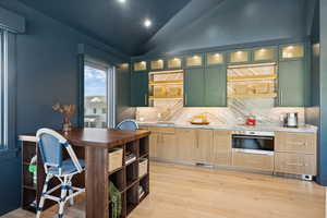 Kitchen with glass insert cabinets, green cabinetry, open shelves, light countertops, and light wood-type flooring