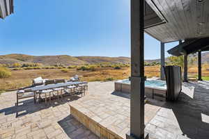 View of patio / terrace featuring outdoor dining area, a hot tub, a mountain view, and a rural view