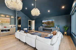 Living area featuring light wood-type flooring, high vaulted ceiling, a glass covered fireplace, a chandelier, and recessed lighting