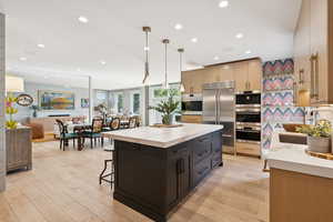 Kitchen with a kitchen bar, decorative light fixtures, stainless steel built in fridge, a kitchen island, and dark cabinets