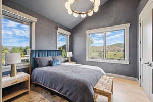 Bedroom with light wood-type flooring, lofted ceiling, wallpapered walls, a chandelier, and a mountain view