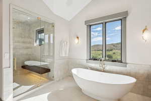Full bathroom featuring a freestanding tub, tile walls, wainscoting, vaulted ceiling, and a stall shower