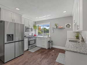 Kitchen featuring decorative backsplash, appliances with stainless steel finishes, white cabinetry, light stone countertops, and dark wood finished floors