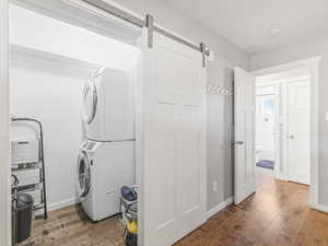 Washroom with estacked washer and dryer, a barn door, and wood finished floors