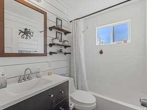 Full bath featuring vanity, shower / bath combo with shower curtain, and wooden walls