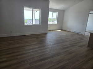 Spare room featuring dark wood finished floors and vaulted ceiling