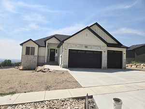 View of front facade with a garage, driveway, board and batten siding, and stone siding
