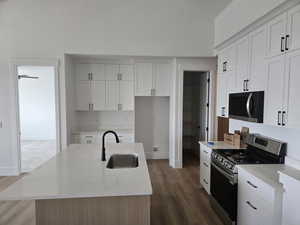 Kitchen with stainless steel appliances, dark wood-style flooring, high vaulted ceiling, a center island with sink, and light stone counters