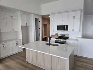 Kitchen featuring stainless steel appliances, an island with sink, white cabinetry, dark wood-type flooring, and light stone countertops