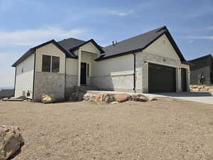 Modern farmhouse style home with stone siding, concrete driveway, an attached garage, a shingled roof, and board and batten siding