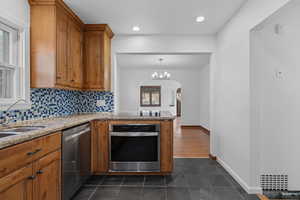 Kitchen with brown cabinetry, appliances with stainless steel finishes, backsplash, arched walkways, and recessed lighting