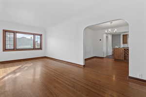 Spare room featuring arched walkways, dark wood finished floors, and a chandelier