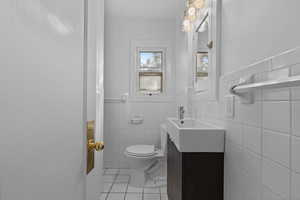 Bathroom featuring light tile patterned flooring, tile walls, vanity, and wainscoting
