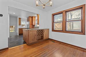 Kitchen featuring dark wood finished floors, a chandelier, brown cabinets, light stone counters, and a peninsula