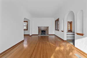 Unfurnished living room with arched walkways, wood finished floors, and a fireplace