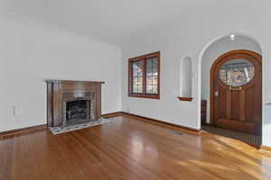 Unfurnished living room featuring wood-type flooring, a fireplace, and arched walkways