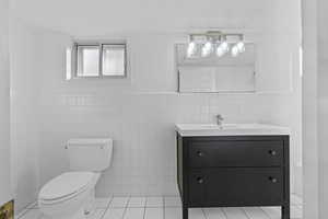 Bathroom featuring tile walls, a wainscoted wall, light tile patterned floors, and vanity